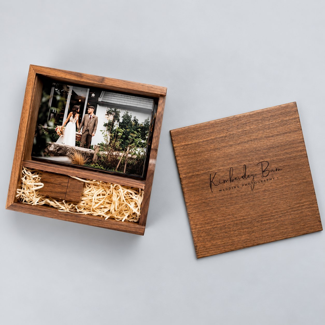Dark walnut wooden USB photo box closed with a 4x6 wedding photo print visible through the lid, and a matching custom engraved 'Kimberley Bam Wedding Photography' USB drive laid beside the box — illustrating the size comparison between a finished wooden gift box and its matching drive.