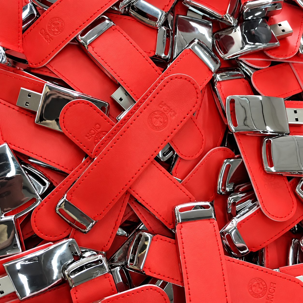 Gövdede krom kaplamalı uç kapaklı ve üzerinde küçük bir kabartma logo bulunan bir yığın kırmızı deri USB bellek; lüks kurumsal hediye veya yönetici promosyonu olarak tipik olarak sipariş edilen premium özel kalıplı bir deri USB tarzını göstermektedir.