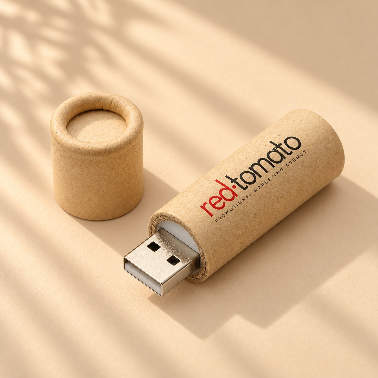 Kapağı çıkarılarak USB konnektörünü ortaya çıkaran, red:tomato promosyon pazarlama ajansı logosuyla markalanmış tek kraft kağıt tüp USB bellek; standart bir dahili sürücünün çevresindeki geri dönüştürülmüş kağıt kasa yapısını gösterir.