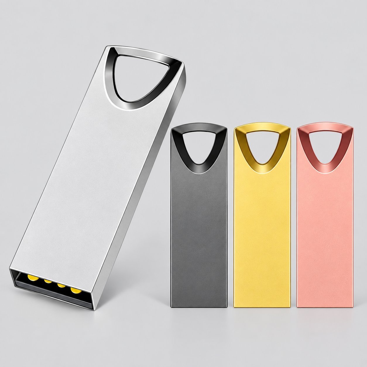 Cuatro memorias USB de metal en forma de cierre trapezoidal con un ejemplo grande de plata al frente y tres unidades más pequeñas negras, de oro y oro rosa detrás, mostrando el cuerpo estilo hebilla usado para sujetar a un llavero.