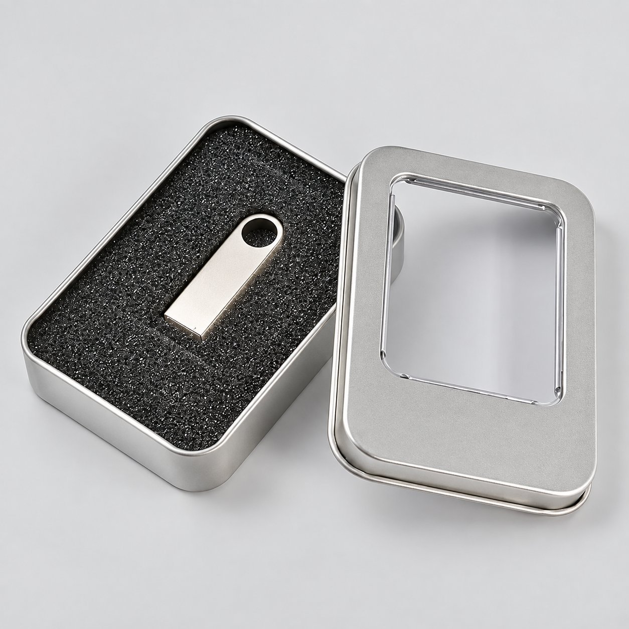 Caja de regalo de lata de metal plateada con inserto de espuma que contiene una sola memoria USB de metal, mostrando la opción de embalaje premium estándar para unidades de USB de metal enviadas como regalo corporativo o set de obsequios.