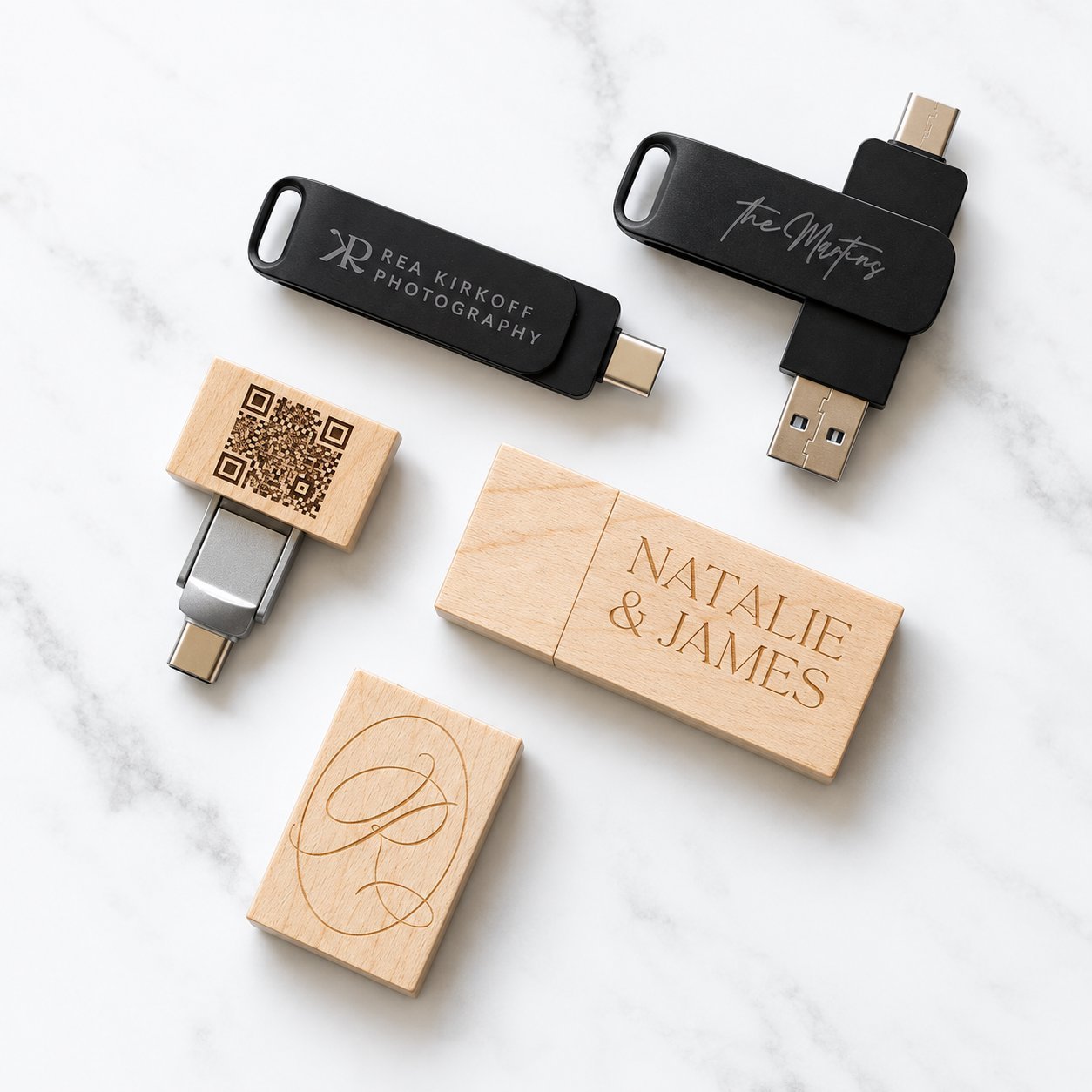 A lineup of light-bamboo wooden USB flash drives in different shapes with brand names and QR codes engraved on each — showing that wood grain and laser-engraved logos vary piece to piece even when the same spec is used across a batch.