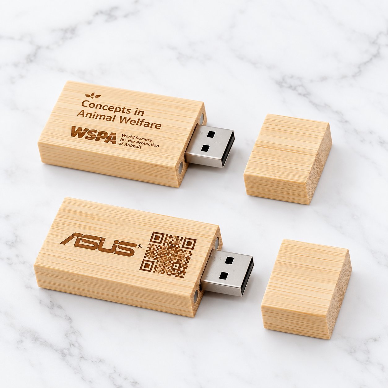 Three wooden USB flash drives on a marble surface — a maple drive engraved with 'Design Unleashed' alongside two light-bamboo drives with engraved QR codes, illustrating the visible wood-grain and tone variation between maple and bamboo even within one product family.