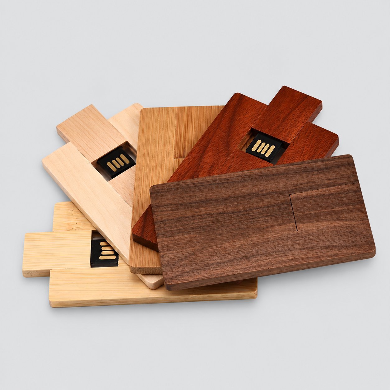 Her biri üstte açıkta bir kayar USB konnektöre sahip, açık akçaağaç, bambu, kiraz ve koyu ceviz kaplamalarda ahşap kart şeklinde bir yığın USB bellek; markalı kurumsal hediyeler için ahşap USB kasa seçeneğini göstermektedir.