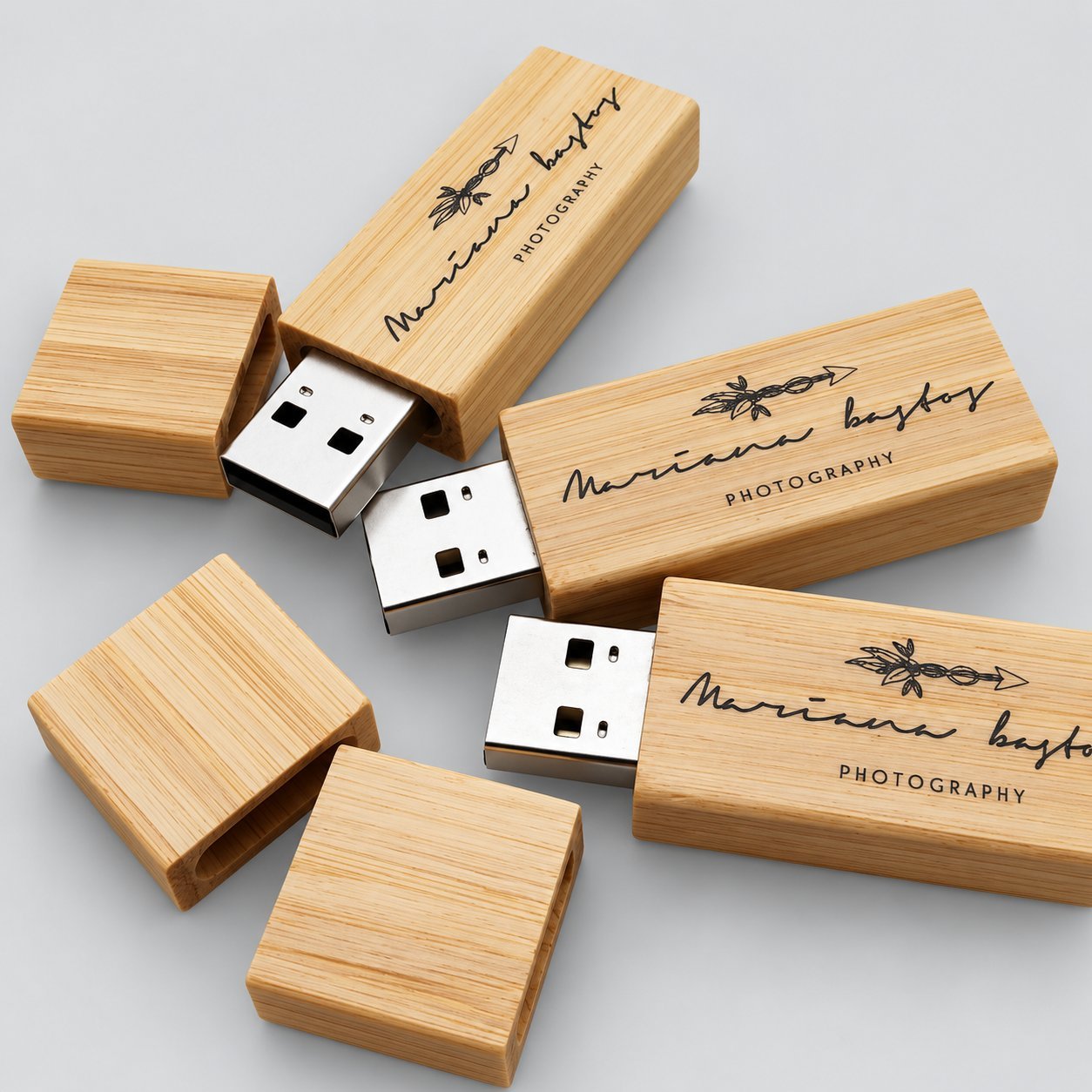 A scattered group of bamboo wooden USB drives with custom laser-engraved logo, several with caps removed to expose the USB-A connector, used as the reference sample for branding durability and approved-sample record-keeping.