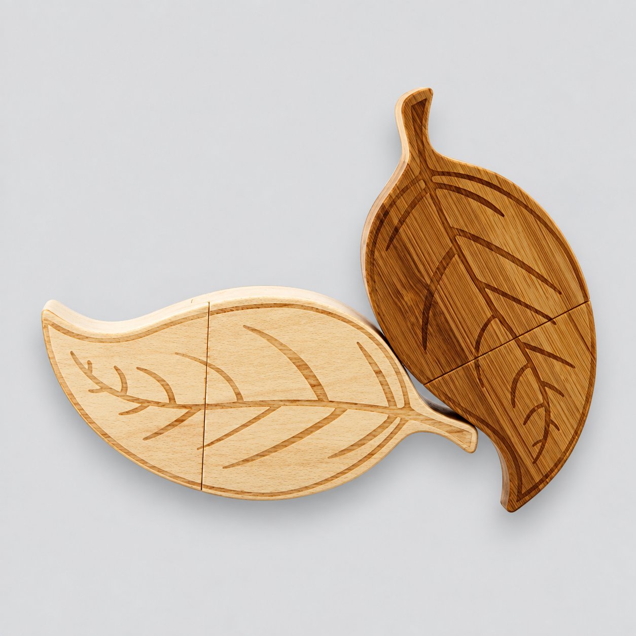 Two custom leaf-shaped wooden USB drives — one in light maple and one in dark walnut — engraved with a leaf vein pattern on each half, illustrating how a non-standard silhouette affects wood-grain variation and visual inspection.