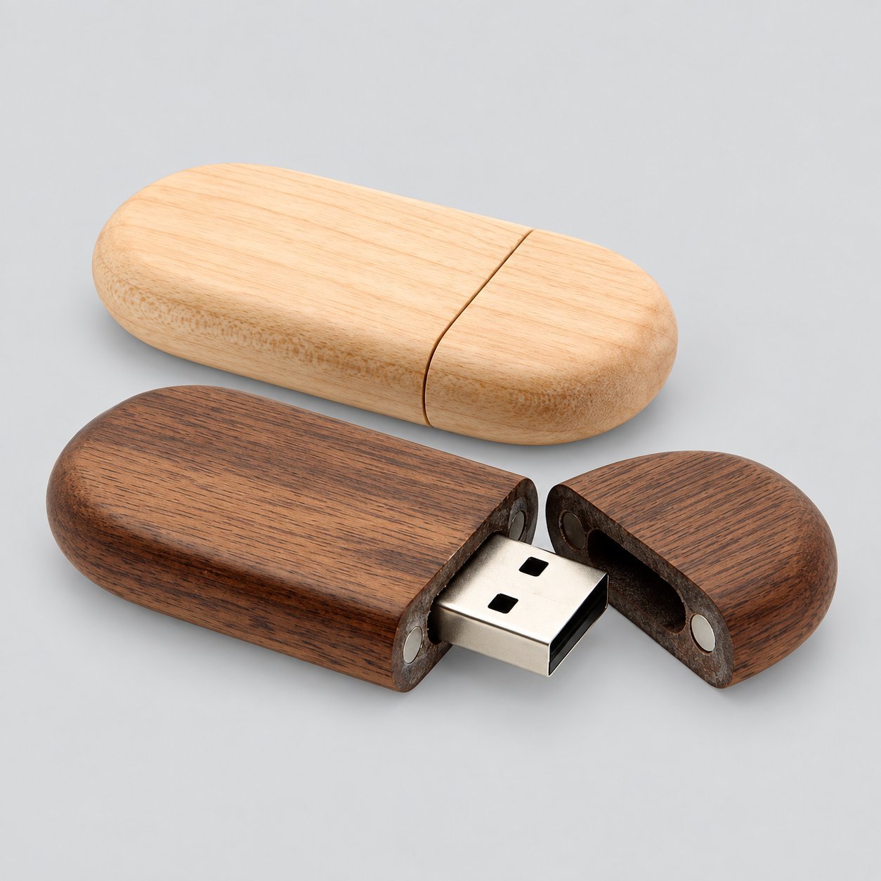 Two oval pill-shaped wooden USB drives — one in light maple and one in dark walnut — with the magnetic cap detached and USB-A connector exposed, showing the wood body wall thickness around the connector that affects port clearance.