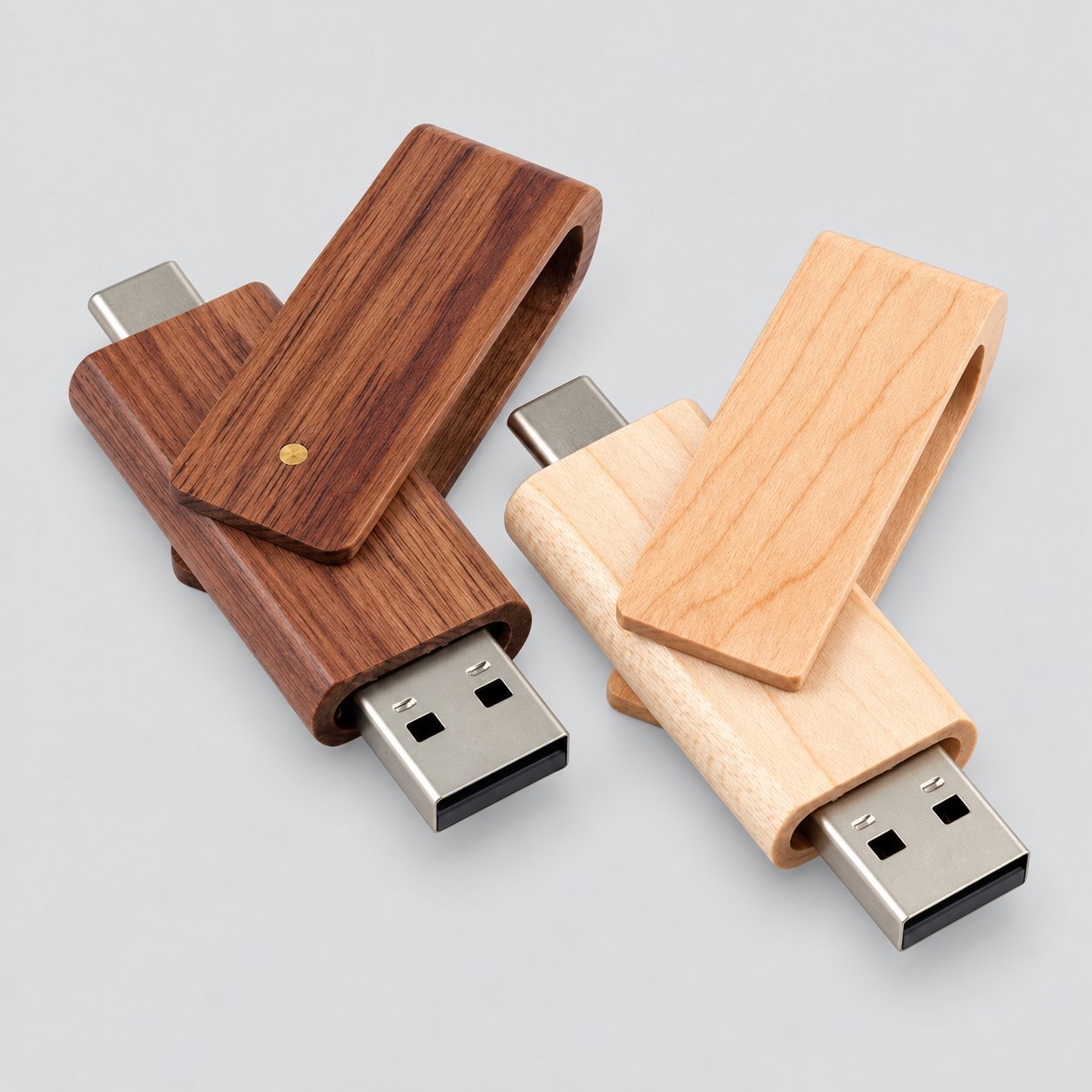 Two swivel-style wooden USB drives side by side — one in dark walnut and one in light maple — with the brass pivot dot visible and USB-A connector exposed, illustrating the cap-free swivel closure that needs to lock open and closed under repeated use.